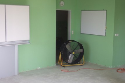 Zapůjčený průmyslový ventilátor v rohu místnosti se zelenými zdmi